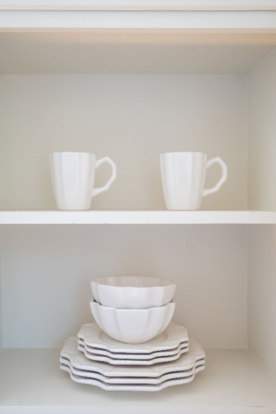 Spotless white cups and plates inside an open kitchen cabinet